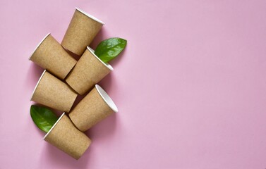 Set of eco-friendly coffee to go cups - kraft paper cups with green leaves above on a pink background. Recycled kraft paper packaging and zero waste concept, mockup. Top view, copy space