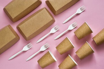 Disposable environmentally eco-friendly food packaging. Brown craft paper containers, drink glasses and forks on a pink background. Top view, flat lay composition