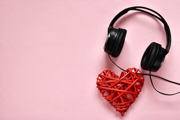 Black headphones with red heart on pink background with copy space. Top view, flat lay. World Music...