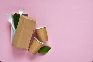 Flat lay composition with disposable eco friendly tableware, plates, cups and green leaves on pink...