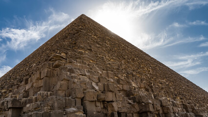 Fototapeta na wymiar The Great Pyramid of Cheops in Giza. A triangular peak on a background of blue sky and clouds. Huge bricks of ancient masonry are visible. Egypt