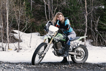 Portrait of an attractive girl sitting on motocross motorcycle off-road with snow on  summer day