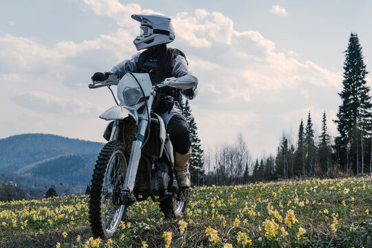 Female wearing moto equipment riding enduro motorcycle  through off-road field with yellow flowers