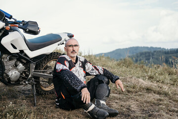 Portrait of 60-year-old Active mature man with grey hair  resting near enduro motorcycle in...
