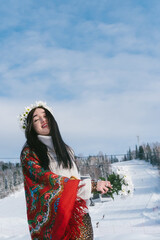 Fototapeta na wymiar Portrait of happy woman wearing traditional red Slavic scarf and wreath of flowers enjoying in ski resort in winter sunny day