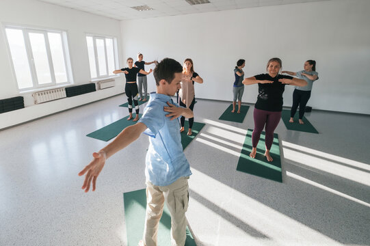 Male Yoga teacher giving lesson to female group in sunny yoga studio