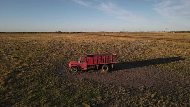 A red old vintage truck standing abandoned in a dry countryside field at sunset. Aerial parallax shot