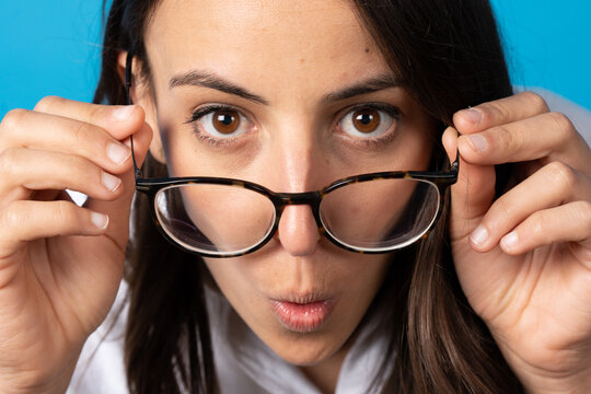 Portrait of surprised pretty hispanic young woman looking over eyeglasses isolated on blue background.