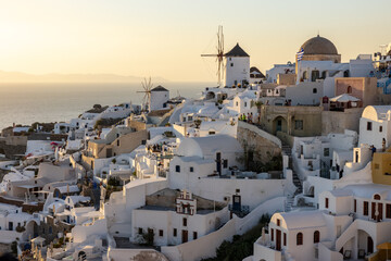  Whitewashed houses and windmills in Oia in warm rays of sunset on Santorini island. Greece