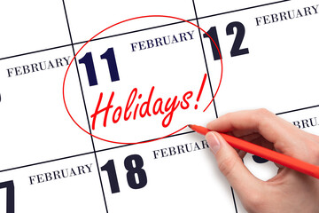 Hand drawing a red circle and writing the text Holidays on the calendar date 11 February. Important date.