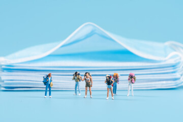 Miniature people travel with face mask on blue background,safety travels