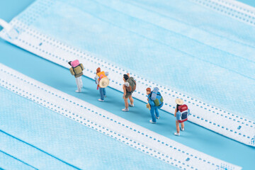 Miniature people travel with face mask on blue background,safety travels