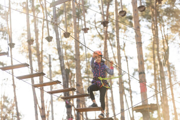 Little girl is standing on a rope, holding a rope with his hands. A child in a rope park passes obstacles