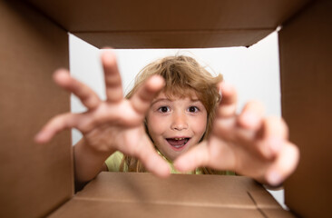 Kid unpacking and opening carton box, and looking inside with surprise face. Child take by hand gift fron open box.