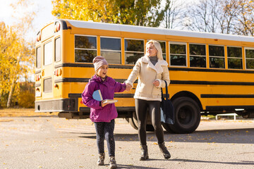 Mother walking her daughter to school bus outside the elementary school.