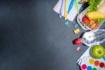 Healthy school lunch box: sandwich, vegetables, fruit, nuts and yogurt with school kids supplies, accessories and backpack on black background flatlay copy space. Back to school concept