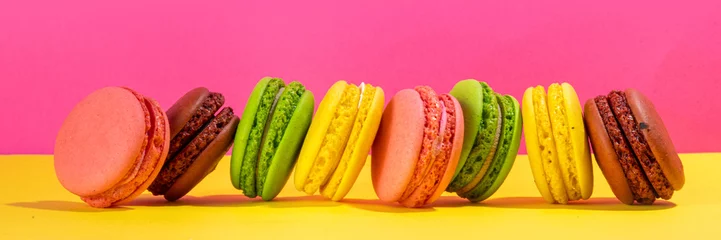  Brigth colorful (yellow, pink, green, brown) various flavor macarons sweet cookies on high-colored pink yellow background. Stack of small french macaron cakes, copy space flatlay © ricka_kinamoto