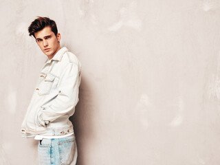 Naklejka na ściany i meble Portrait of handsome confident stylish hipster lambersexual model.Man dressed in jacket and jeans. Fashion male posing in studio near grey wall