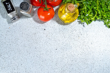Spices (black pepper, garlic, onion), greens, olive oil and tomatoes. Ingredients for cooking. On the white stone concrete table top view copy space.