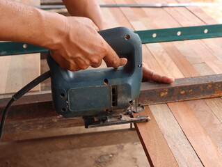 A carpenter uses a green jigsaw to cut wood.