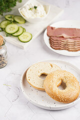 An empty bagel cut in half: ingredients for sandwich with pastrami, cucumber slices, watercress salad and ricotta on marble background