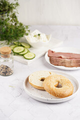 An empty bagel cut in half: ingredients for sandwich with pastrami, cucumber slices, watercress salad and ricotta on marble background