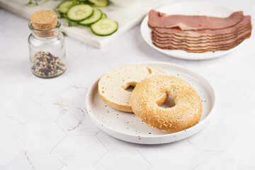 An empty bagel cut in half: ingredients for sandwich with pastrami, cucumber slices, watercress salad and ricotta on marble background
