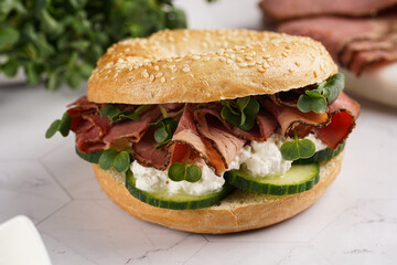 A bagel sandwich with pastrami, cucumber slices, watercress salad and ricotta on marble background