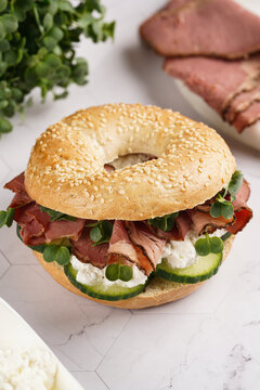 A bagel sandwich with pastrami, cucumber slices, watercress salad and ricotta on marble background