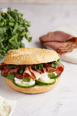 A bagel sandwich with pastrami, cucumber slices, watercress salad and ricotta on marble background