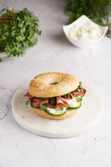 A bagel sandwich with pastrami, cucumber slices, watercress salad and ricotta on marble background