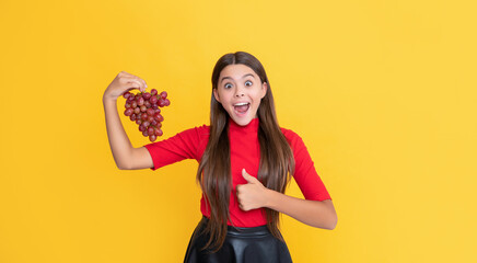 amazed positive teen kid hold bunch of grapes on yellow background