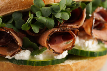 A bagel sandwich with pastrami, cucumber slices, watercress salad and ricotta on marble background,...