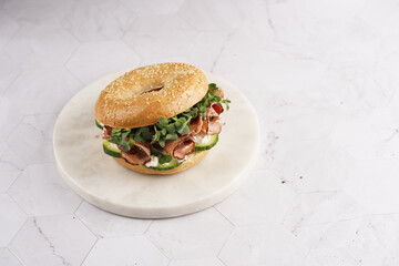A bagel sandwich with pastrami, cucumber slices, watercress salad and ricotta on round marble board