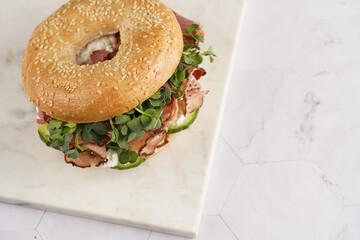 A bagel sandwich with pastrami, cucumber slices, watercress salad and ricotta on square marble board