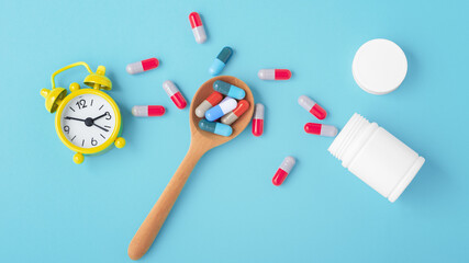 Medicine time concept with capsule pills on spoon and alarm clock