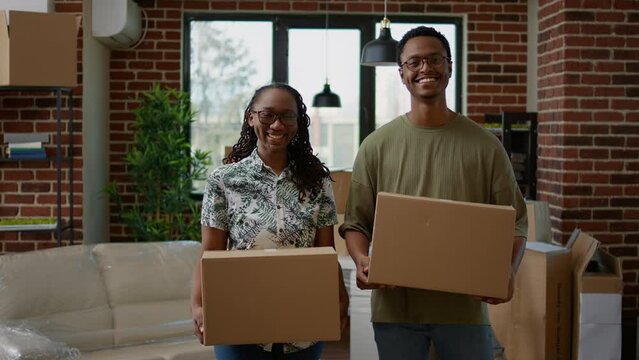 Portrait of african american couple holding cardboard boxes, moving in new apartment flat. Married homeowners relocating together in new home, loan and mortgage household, moving day.