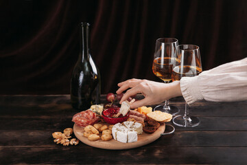 Woman's hand takes a piece of cheese from the Appetizers board with assorted cheese, meat, sausage...