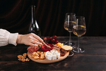 Woman's hand takes a piece of cheese from the Appetizers board with assorted cheese, meat, sausage...
