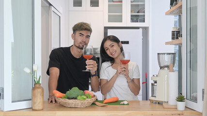 Lovely young couple preparing healthy food and drinking wine at home kitchen.