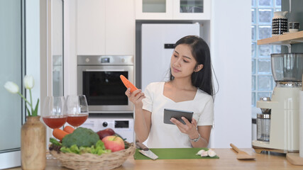 Smiling young asian woman reading online recipe on digital tablet and preparing vegetarian meal in the kitchen.