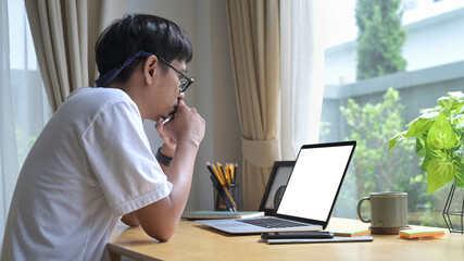 Thoughtful asian male freelancer working at home with laptop computer.