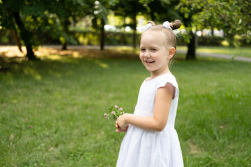 funny smiling kid girl in white dress with spring flowers in green park