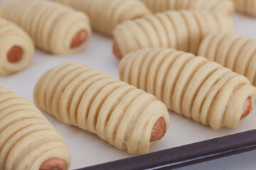 An uncooked sausage bread roll or hotdog bun dough rising on a baking tray preparing to put in oven. A bread made of a mix of flour, milk, water, sugar, salt, active dry yeast, and butter