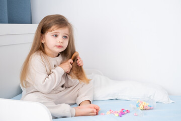 little kid girl with blonde long hair combing her hair with wooden comb