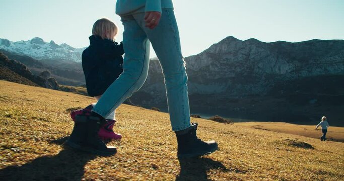 Hiker family walk on mountain at the sunset. Mother holding her daughters hand on vacation trip. Traveler woman with children exploring epic nature landscapes. Cinematic footage with lens flares