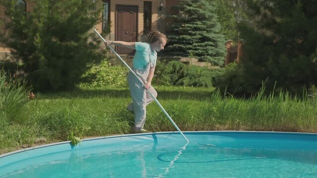 Woman cleaning lady with underwater vacuum cleaner cleans swimming pool collecting garbage from bottom.