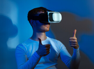 Modern young man experiencing virtual reality glasses in futuristic neon illuminated studio