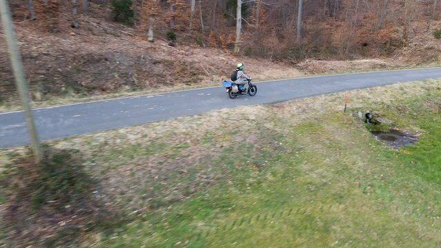Aerial footage of a person on a motorbike driving along a narrow forest road. Wide angle following shot