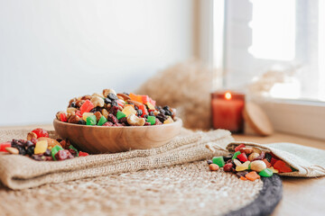 Wooden plate with candied fruits and dried fruits on a wicker stand against the background of a candle, eco concept